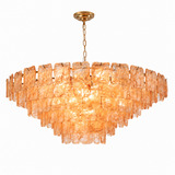 Illuminated chandelier with tiered amber textured glass panels and a gold chain and ceiling canopy against a white background.