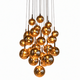 Chandelier with amber-tinted globes glowing on slender dark cables at staggered heights against a white background.