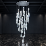 A modern multi-light chandelier with clear textured glass rods hanging from a circular chrome ceiling mount, shown suspended in a dark, minimalist room with a polished marble floor.