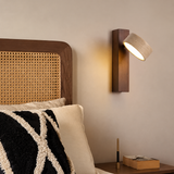 Wall sconce with a beige travertine shade and walnut-finish wood backplate, glowing beside a woven cane headboard.