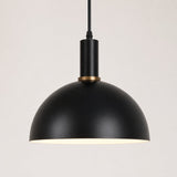 A modern black dome pendant light with a warm brass accent ring and a glowing white interior, suspended by a black cord against a light gray background.