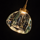 Chandelier close-up showing an illuminated clear crystal drop with a gold-toned cap against a black background.