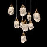 A nine-light chandelier features textured clear crystal shades with gold caps suspended at varying heights against a black background.