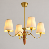 A five-light brass chandelier with pleated white fabric shades, shown illuminated against a neutral gray background.