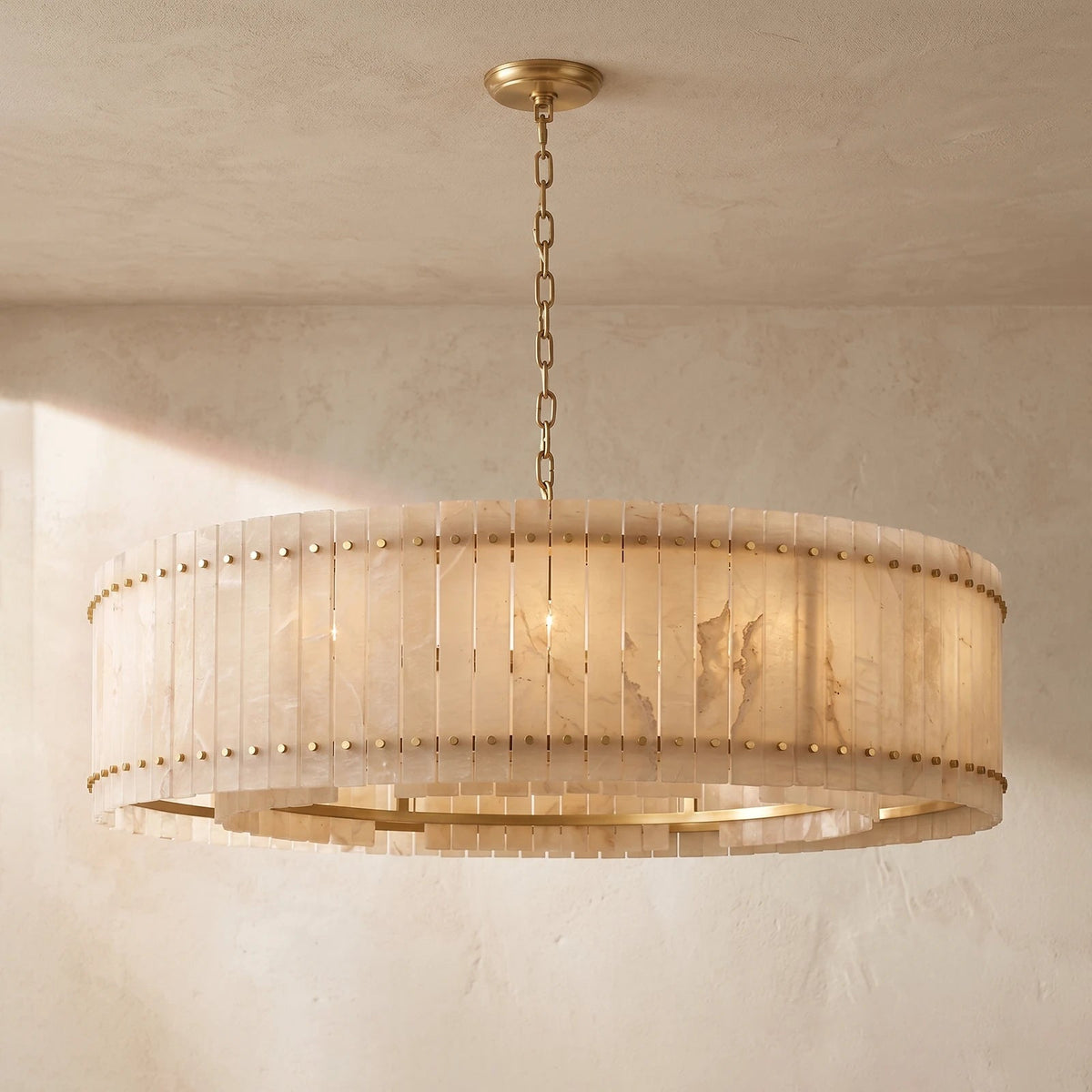 A large circular chandelier with a warm brass frame and a translucent beige shell shade, hanging from a chain in a textured beige room.