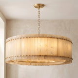 A large drum-shaped chandelier with a warm glowing beige translucent shade and gold-toned metal hardware, hanging from a chain in a neutral interior setting.