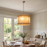 A round chandelier with glowing cream alabaster panels hangs above a set dining table beside glass garden doors.