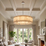 A large circular pendant chandelier with a warm beige woven drum shade and silver-toned metal hardware hangs in a bright, elegant living room with coffered ceilings, large windows, and a fireplace.