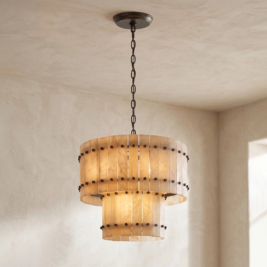 Illuminated two-tier chandelier with cream alabaster panels and dark metal fittings hangs from a dark chain in a neutral room.