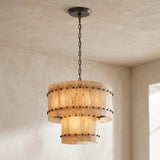 Illuminated two-tier chandelier with cream alabaster panels and dark metal fittings hangs from a dark chain in a neutral room.