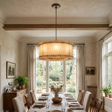 A wide round alabaster chandelier hangs above a long dining table beneath a wooden ceiling beam.