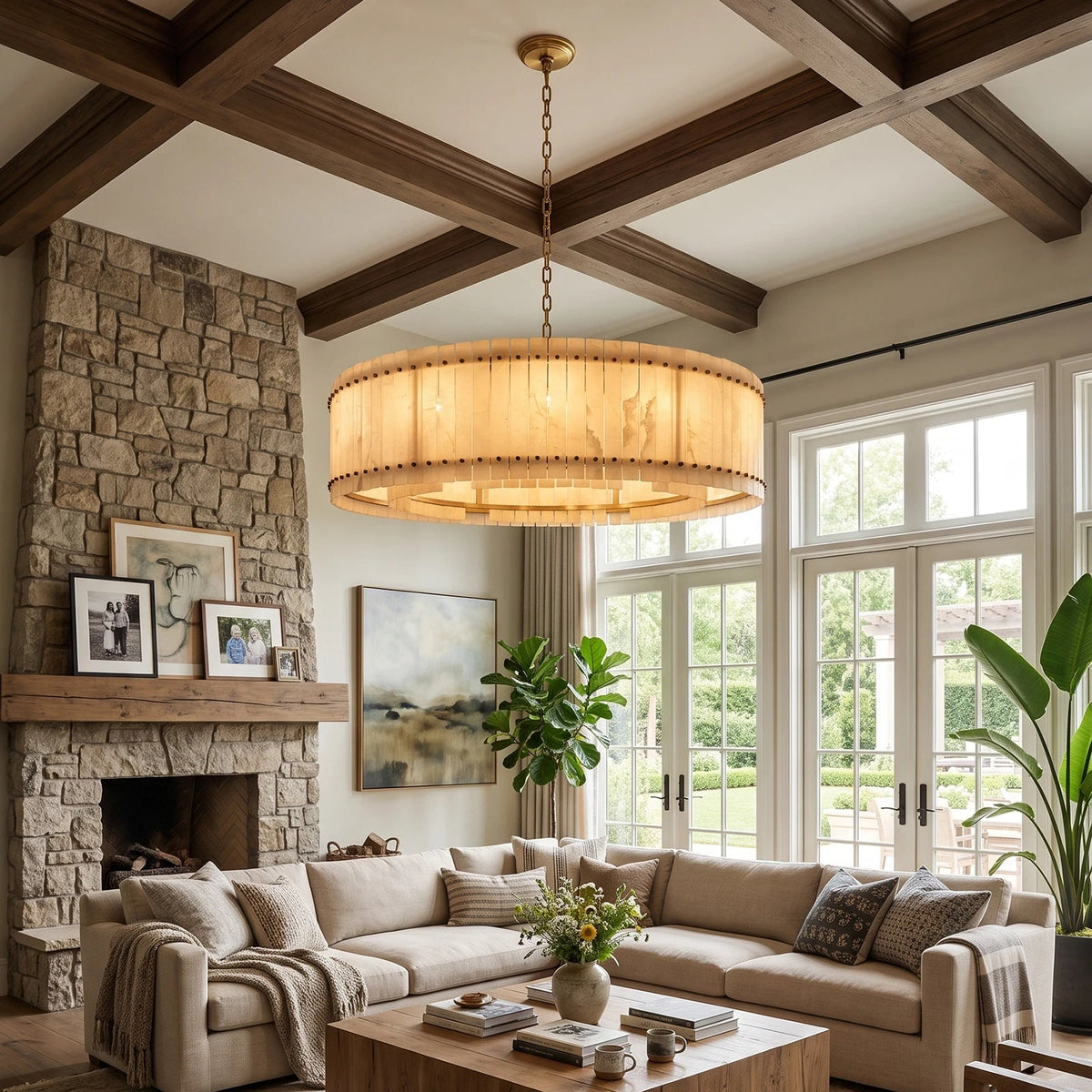 A wide round alabaster chandelier with brass hardware hangs in a living room beneath dark ceiling beams beside a stone fireplace.