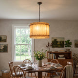 A round chandelier with glowing cream alabaster panels hangs above a round wooden table surrounded by spindle-back chairs.