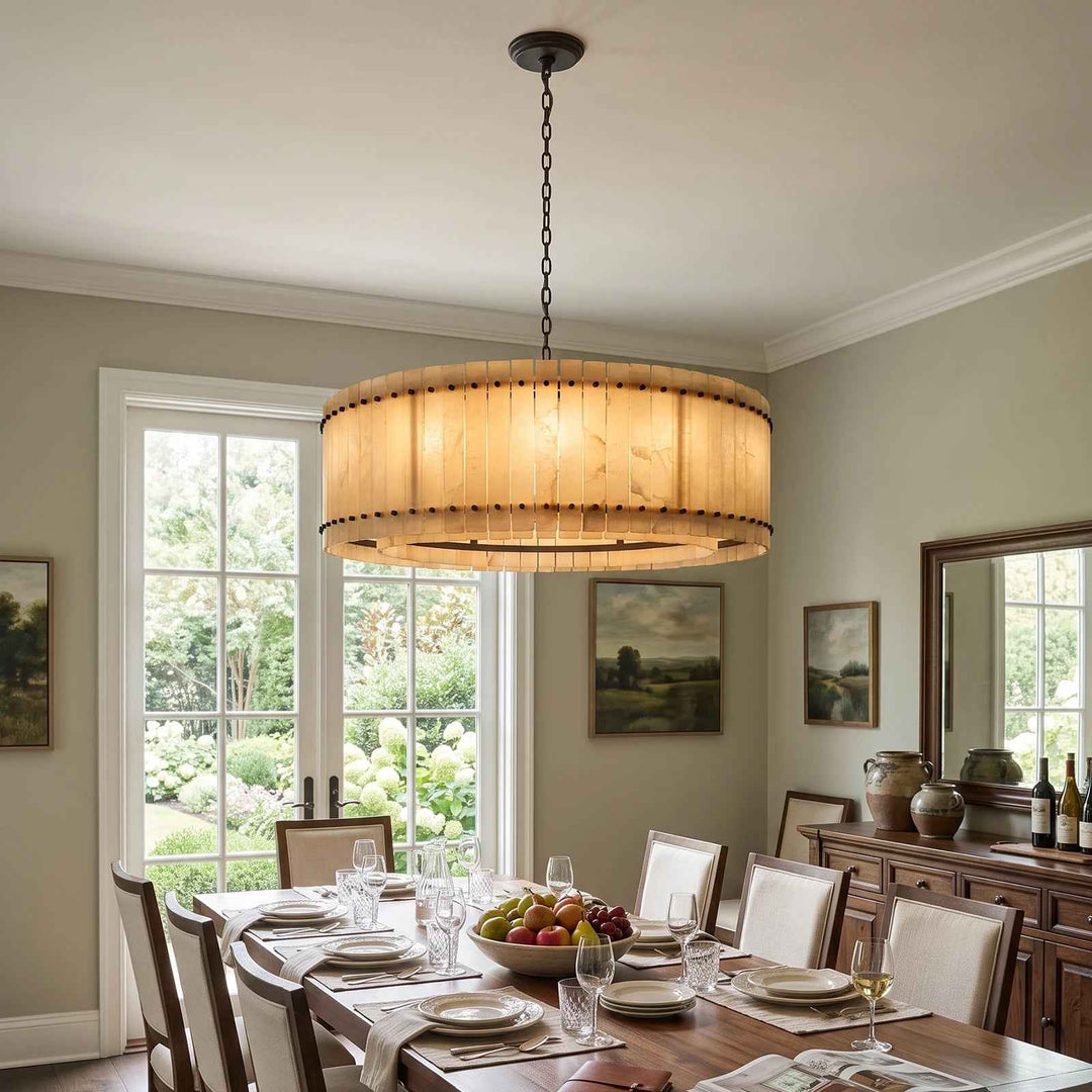 A wide round chandelier with cream alabaster panels hangs over a long wooden dining table near a sideboard and mirror.