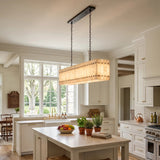 A linear chandelier with glowing cream alabaster panels and dark suspension chains hangs above an island in a white kitchen.