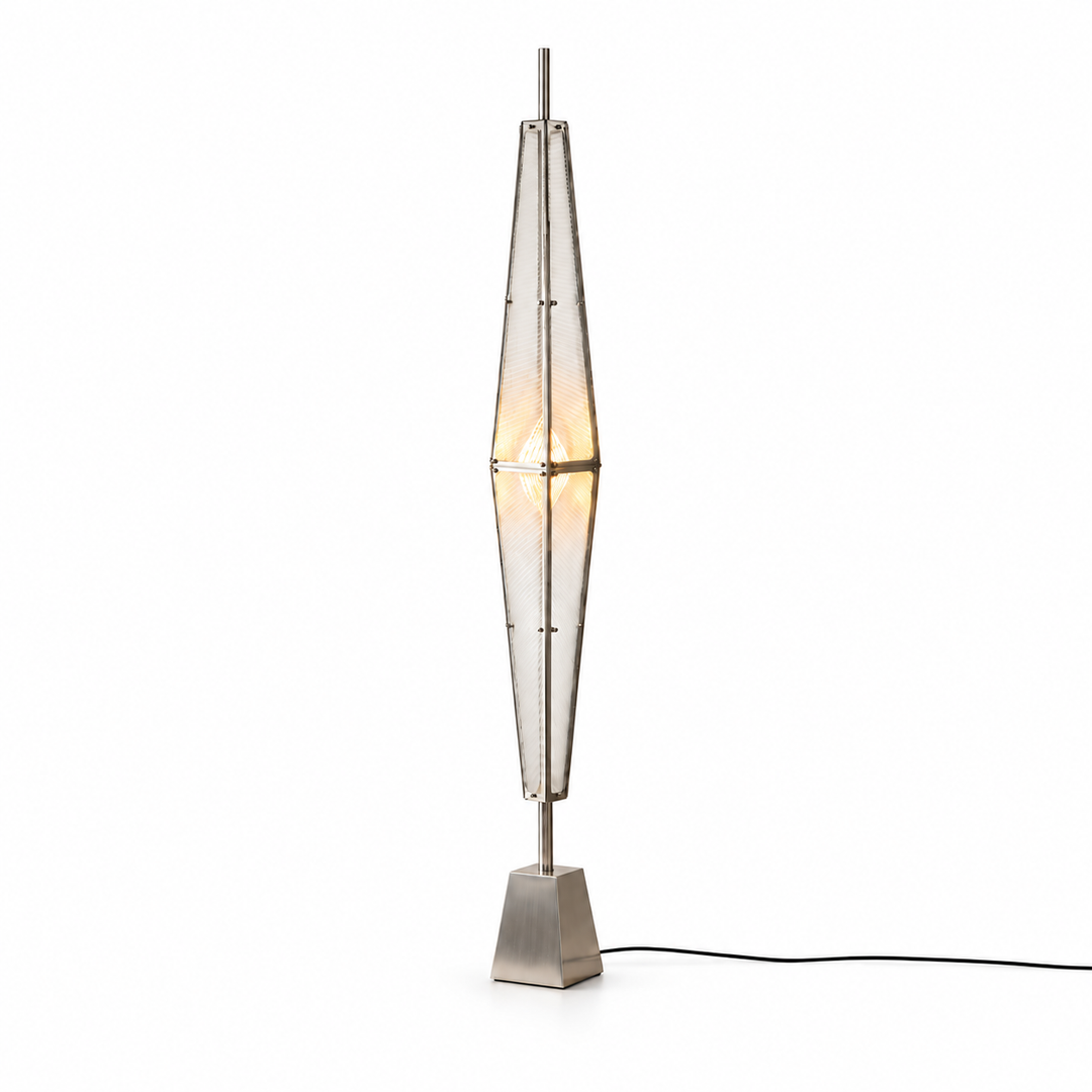 Silver floor lamp with a tall prism-shaped acrylic shade, warm central glow, tapered metal base, and black cord against a white background.