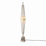Silver floor lamp with a tall prism-shaped acrylic shade, warm central glow, tapered metal base, and black cord against a white background.