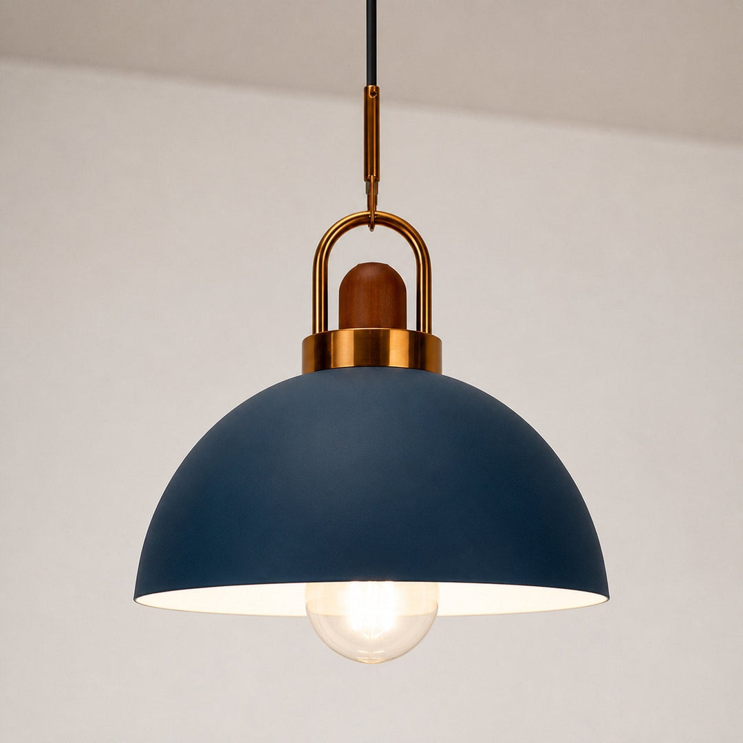 A modern dome-shaped pendant light with a matte navy blue shade, a warm brass metal hanger, and a glowing clear bulb, suspended against a neutral off-white wall.