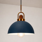 A modern dome-shaped pendant light with a matte navy blue shade, a warm brass metal hanger, and a glowing clear bulb, suspended against a neutral off-white wall.