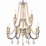 A multi-tiered chandelier with a distressed dark metal frame, cream-colored carved accents, hanging bead strands, and candle-style bulbs, shown against a plain white background.