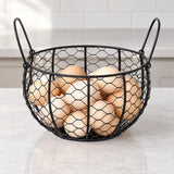 Black wire egg basket with raised side handles, holding eggs on a counter.