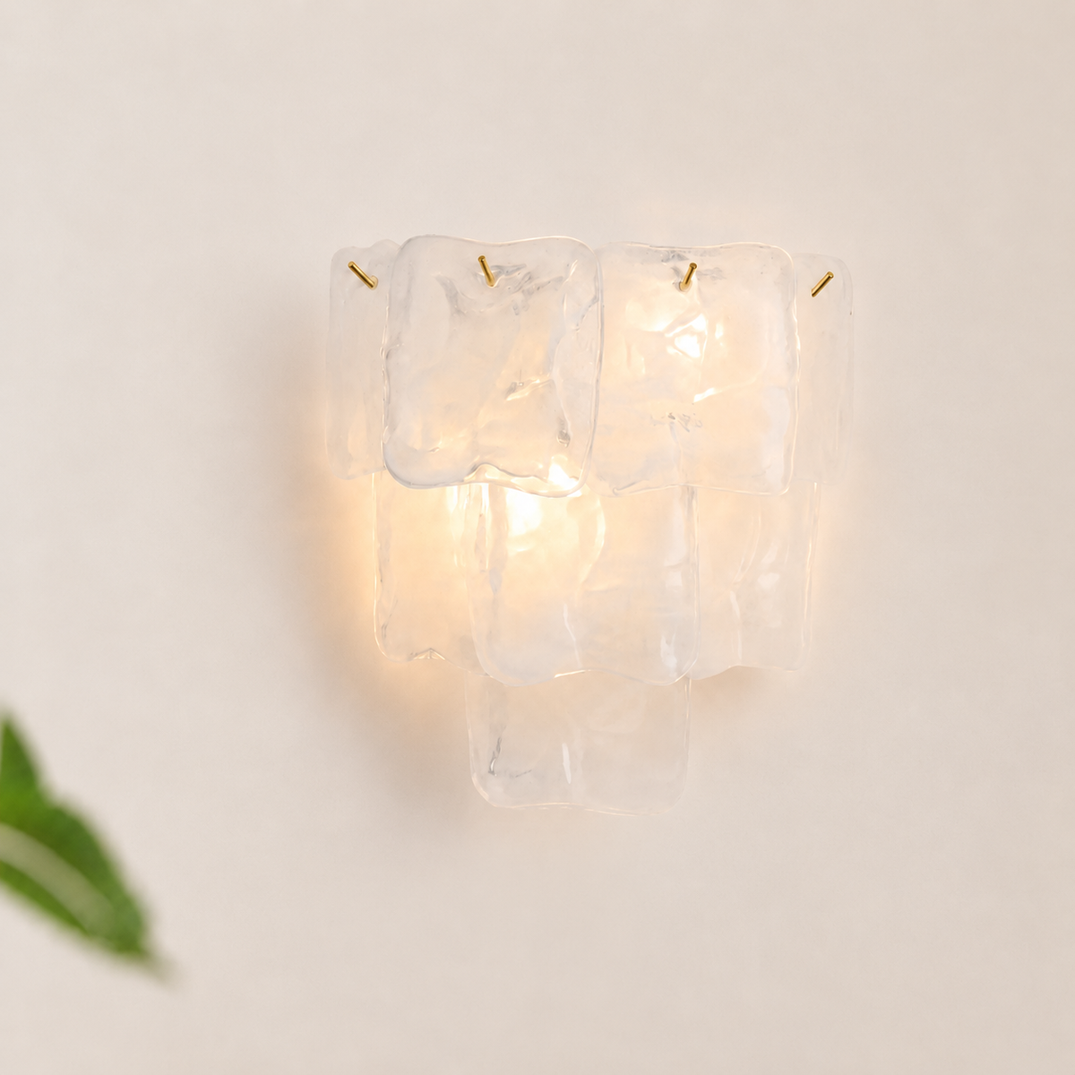 A modern wall sconce light fixture made of stacked, irregular clear acrylic or glass blocks, glowing with a warm yellow light against a plain off-white wall.