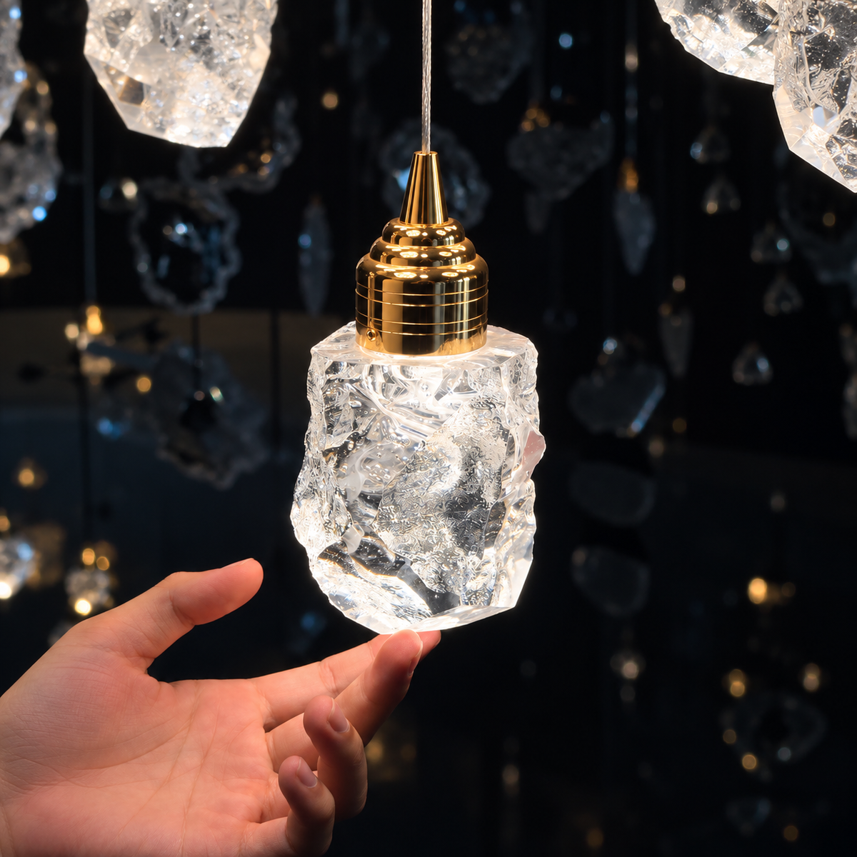 A hand supports one illuminated clear crystal shade of the chandelier, showing its irregular texture and polished gold cap against a dark background.