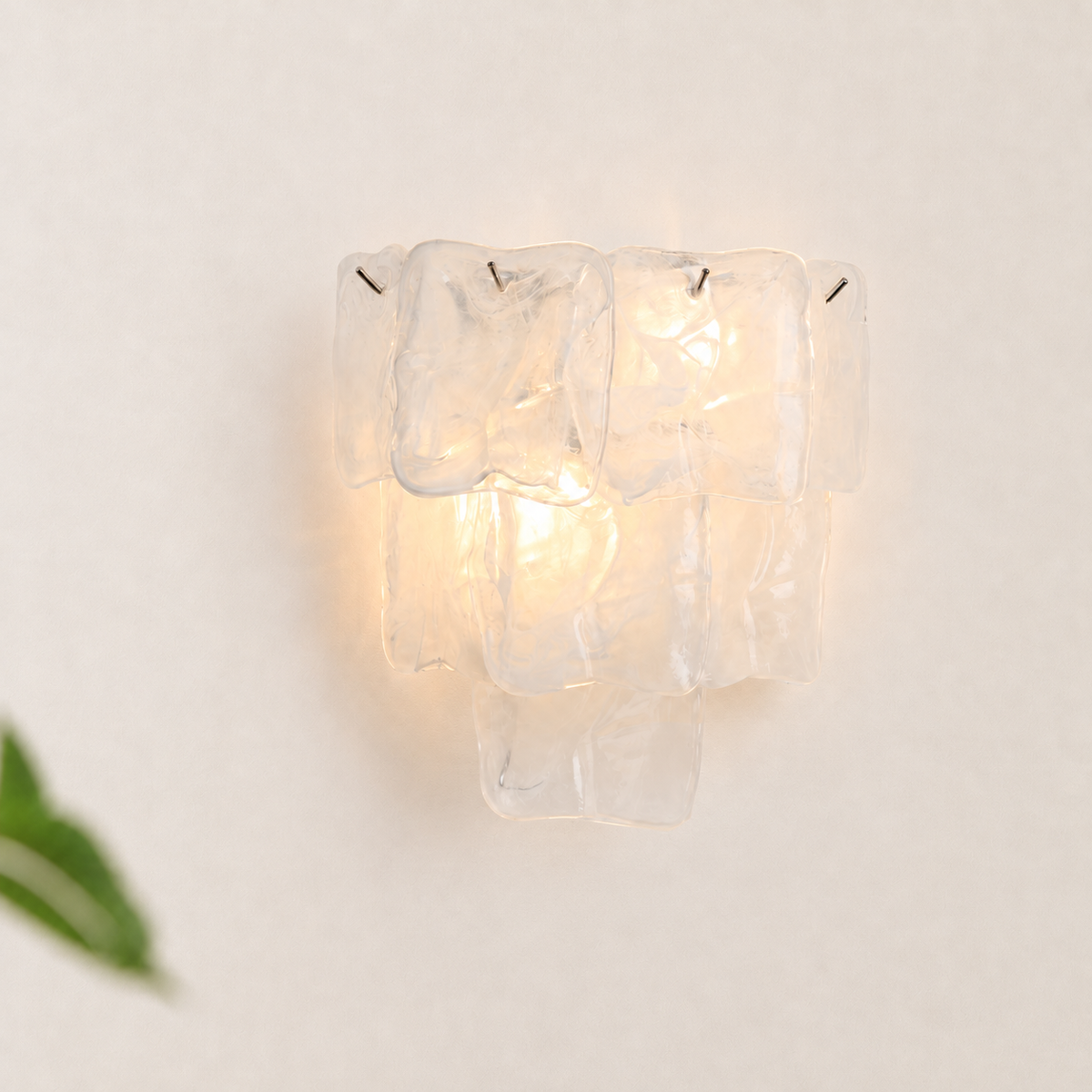A modern wall sconce featuring a cluster of clear, textured glass blocks that glow warmly from an internal light source, mounted on a plain off-white wall.