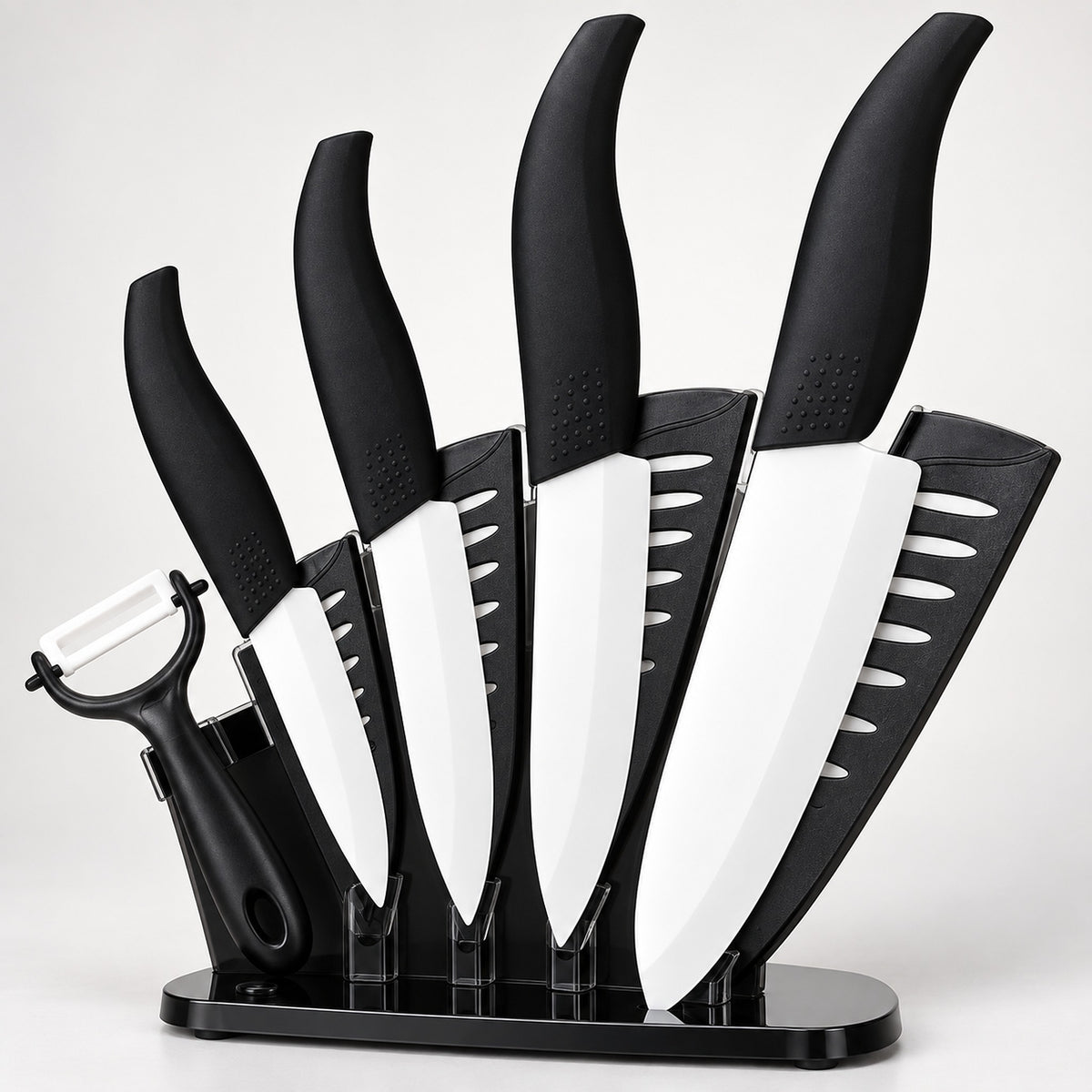 A 5-piece kitchen knife set with black handles and white blades, displayed in a black stand with a black peeler attached, on a light gray background.