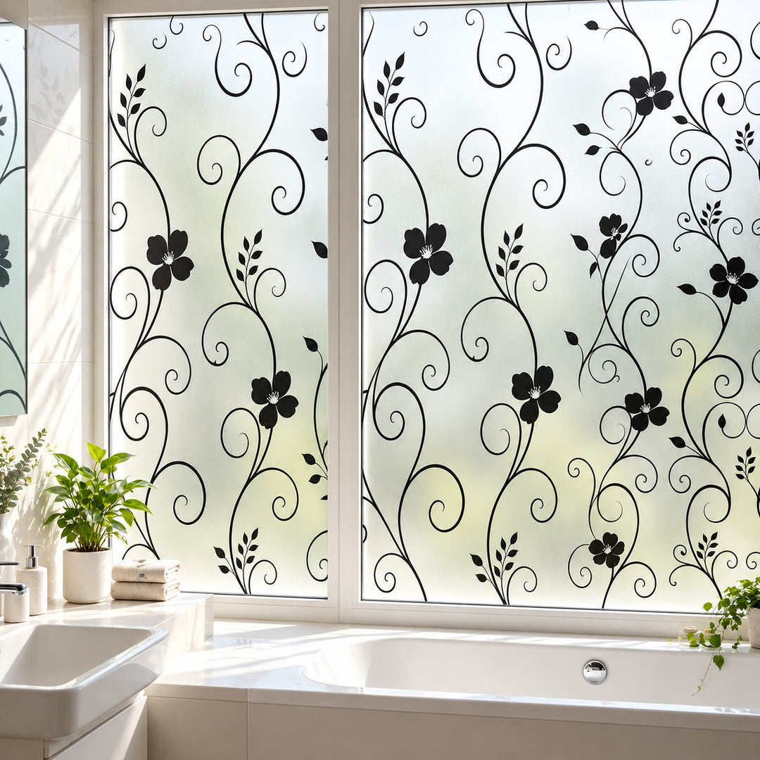 Black floral scroll vine window film applied to frosted glass panels in a bright bathroom, with a bathtub, sink, and potted plants visible.