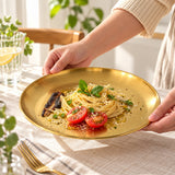 Gold shallow stainless steel serving plate carrying pasta at a dining table.