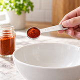 Stainless-steel 5 ml measuring spoon holding paprika above a mixing bowl.