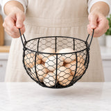 Hands carrying a black wire egg basket by its two folding side handles.