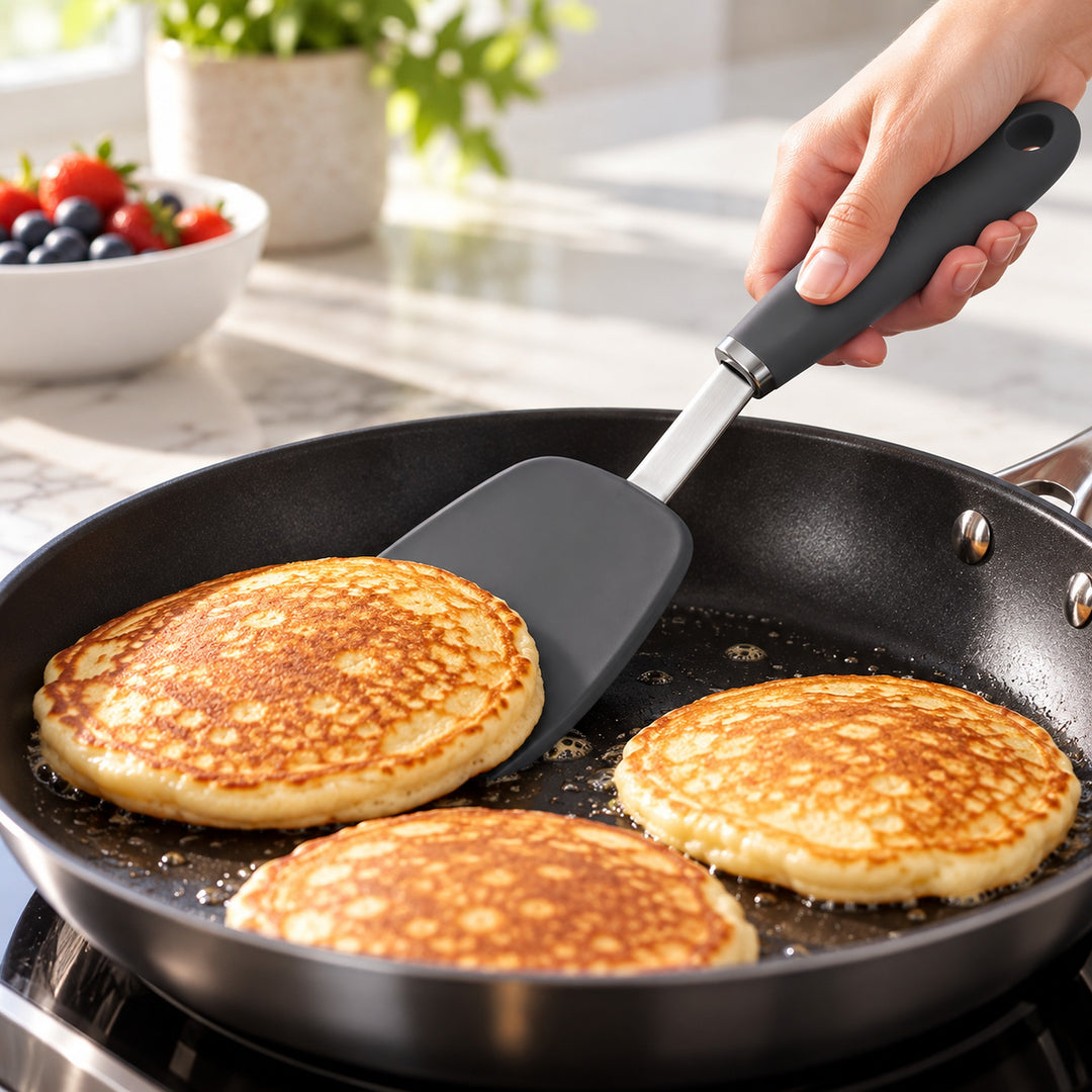 Charcoal silicone turner lifting a pancake in a nonstick skillet.