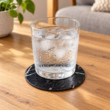 Black marble-print coaster under a chilled glass, keeping condensation off the wooden table.