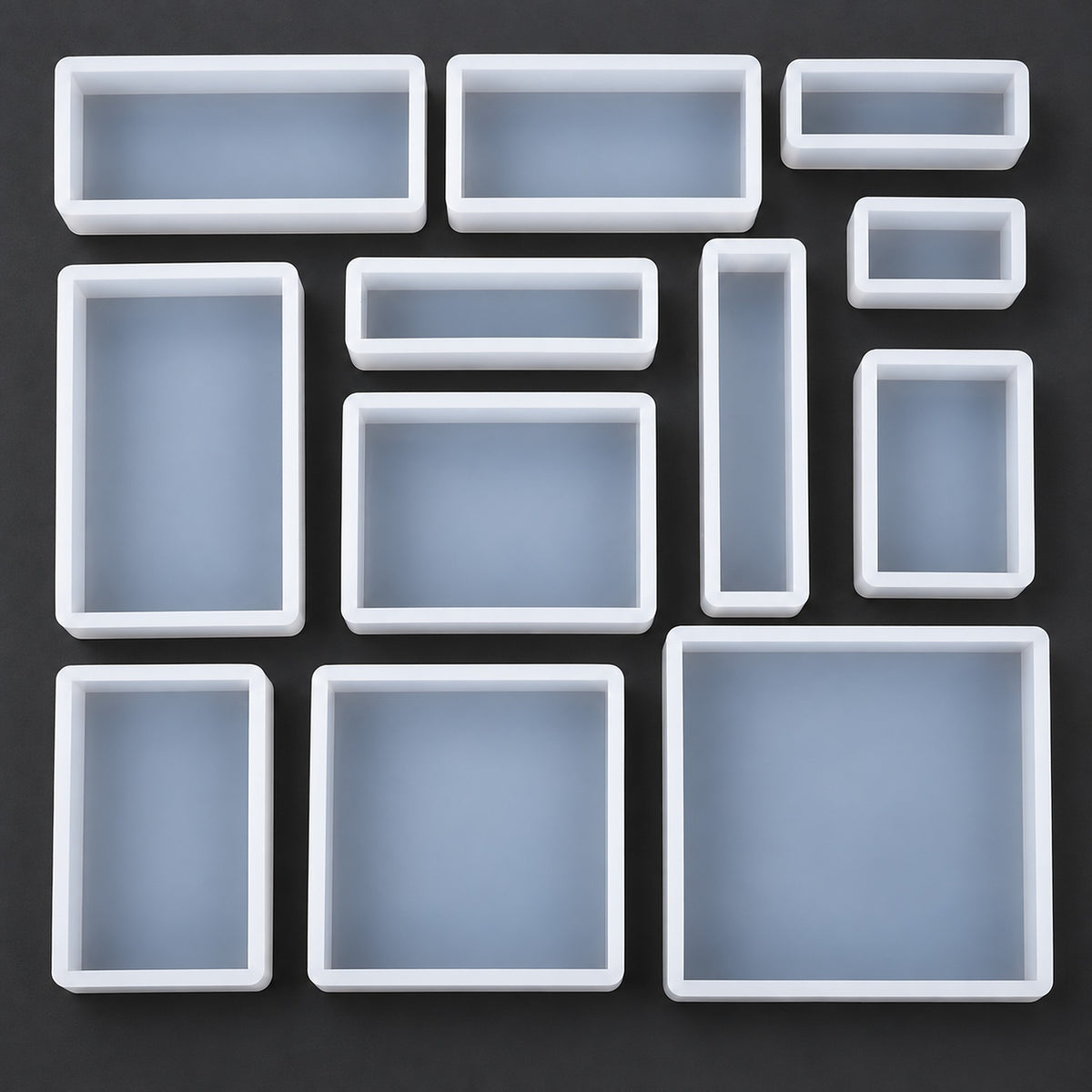 A set of white rectangular silicone mold cavities in various sizes, arranged neatly on a dark gray background.