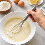 Stainless balloon whisk mixing batter by hand.