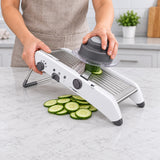 White mandoline preparing cucumber slices with its food holder.