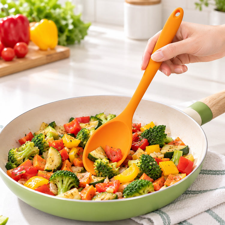 Orange medium silicone spoon stirring vegetables in a pan.