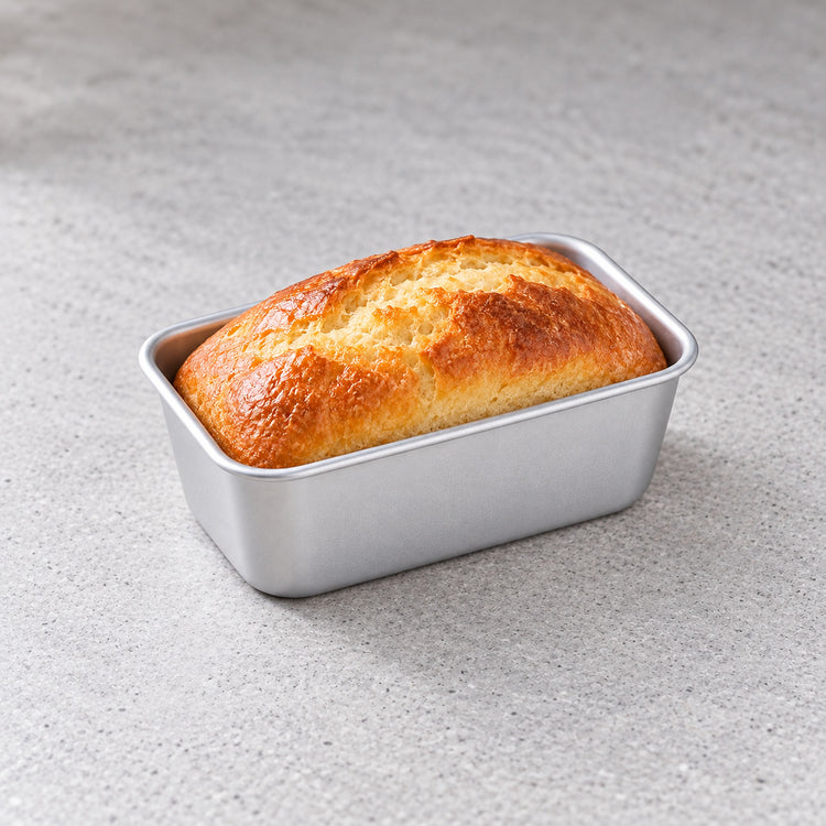 Mini aluminum loaf pan holding a small homemade bread loaf.