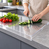 Clear acrylic cutting board hooked over the counter edge during cucumber preparation.