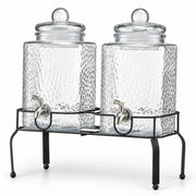 Two clear glass canisters with a hammered texture, each with a lid and a metal spout, displayed on a black metal stand against a white background.