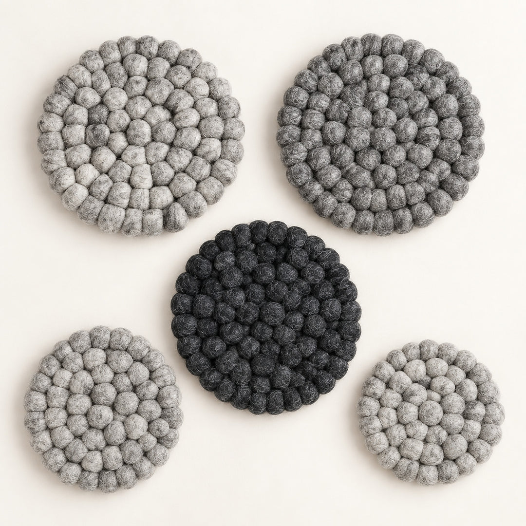 Five round felt coasters with a textured bumpy knit pattern, arranged on a light cream background. Four coasters are light gray and one is dark charcoal black.