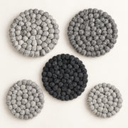 Five round felt coasters with a textured bumpy knit pattern, arranged on a light cream background. Four coasters are light gray and one is dark charcoal black.