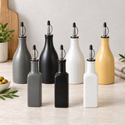 Six matte ceramic oil and vinegar bottles in gray, black, white, and mustard yellow, arranged on a light marble countertop with a neutral background.