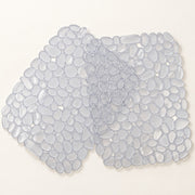 A translucent pebble-shaped mat made of many small rounded semi-clear pieces, arranged in an irregular organic shape on a plain light beige background.