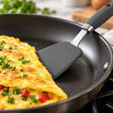 Thin silicone edge sliding beneath an omelet; stainless-steel shaft visible.