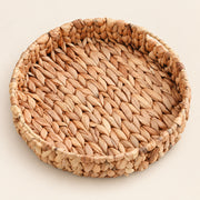 A round woven tray made from natural seagrass or straw, shown from a top-down view on a light beige background.