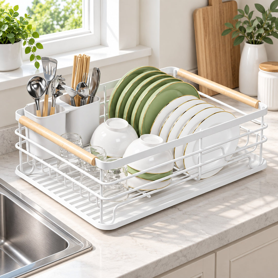 A white wire dish drying rack with light wood handles sits on a kitchen counter next to a sink, holding green and white plates, bowls, and utensils.