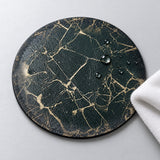 Black and gold artificial-leather coaster showing textured grain, water beads and a wiping cloth.